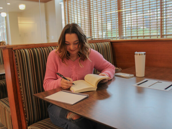 Laci Thompson sitting at a table writing on a book