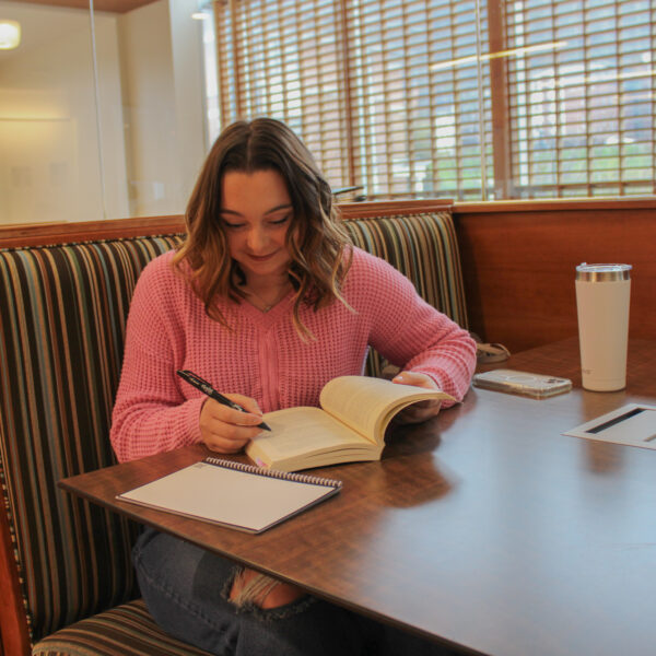 Laci Thompson sitting at a table writing on a book