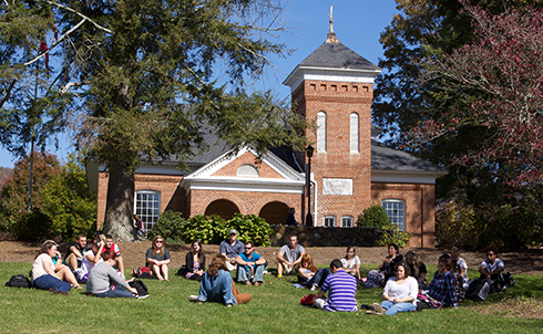 a group of people sitting on grass in front of a brick building